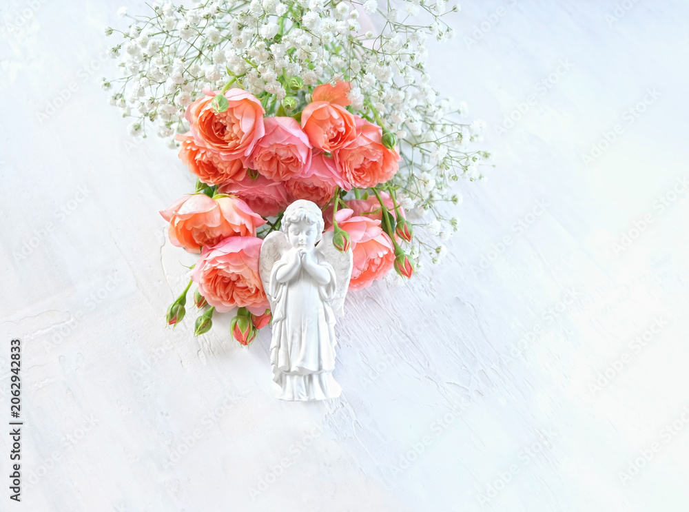 Obraz premium Beautiful praying angel figurine with bouquet of rose and gypsophila flowers on light abstract background. Religious church holiday. symbol of faith in God, pray, believe, christianity. flat lay