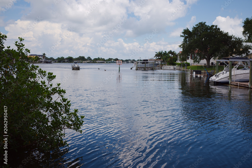 Fototapeta premium Calm Residential Waterfront With Boats, Private Docks and Cloudy Sky Over a Tranquil Bay Crisp Park in St. Petersburg, FL conveying peaceful coastal living, leisure boating and relaxed summer atmosphe
