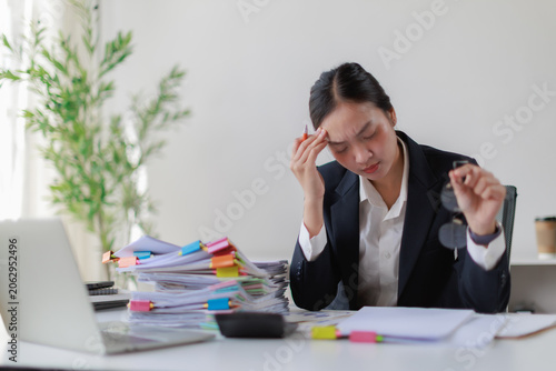 Young Asian businesswoman sitting at her office desk. Holding her head with one hand due to a severe headache caused by stress and overwork