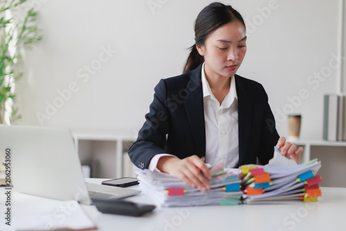Canvas Print Asian businesswoman managing stacks of financial documents and paperwork on an o