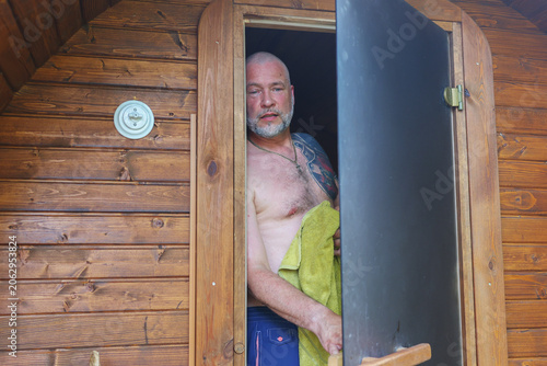 Smiling man after a sauna session in a wooden outdoor sauna, promoting relaxation, recovery and self-care.