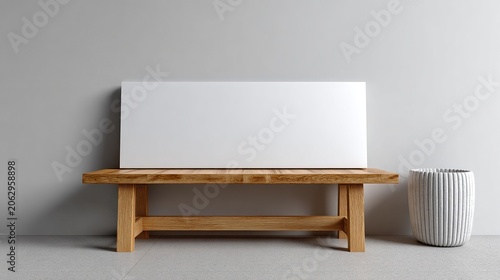 Blank Canvas on Wooden Bench: A minimalist composition featuring a blank white canvas resting on a rustic wooden bench, beside a contemporary ribbed planter, set against a clean, light gray wall.