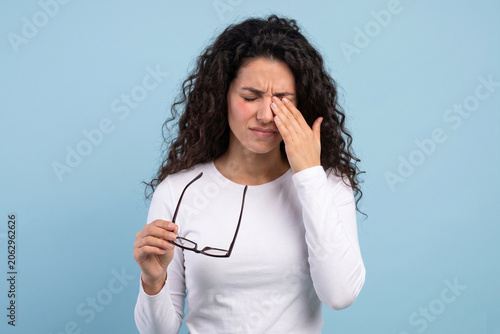Young woman holding glasses and rubbing her eye experiencing eye strain and fatigue