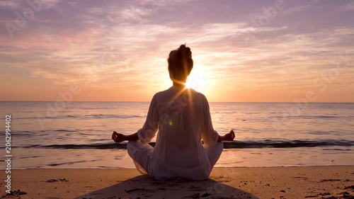 Serene woman meditating on a beach at sunset with a warm glow, sitting in lotus position with hands in a peaceful gesture.