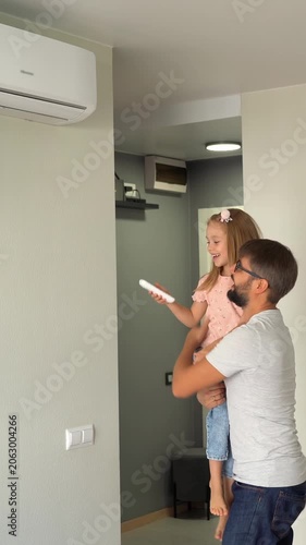 Father kept to hand little daughter and turn on air conditioner using remote control. Happy family adjust comfortable temperature of cooler system. Vertical shot