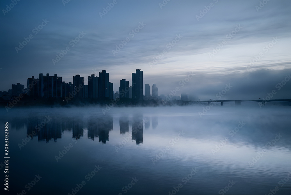 Fototapeta premium Han River Misty Dawn – Seoul Skyline Silhouette Reflected in Foggy Water
