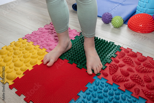 Child walking barefoot across orthopedic massage mats with different tactile textures. Concept of sensory integration, balance development, coordination, motor skills, foot health.