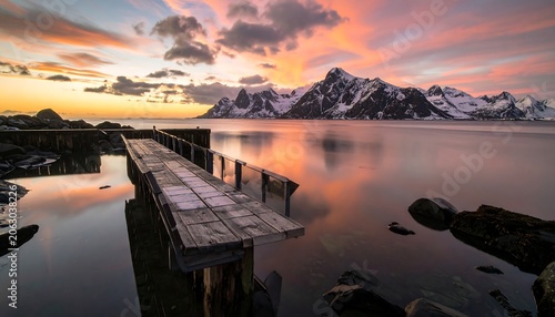 Wooden Pier Extending Toward Snowy Mountain Range at Colorful Arctic Sunset