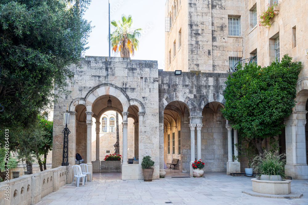 Fototapeta premium Jerusalem, Israel, June 13, 2026. An outdoor stone courtyard with arched arcades where a photographer stands taking a picture of the historic architecture. International YMCA