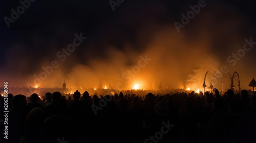 Crowd gathered in silhouette against a vibrant predawn mist filled with numerous glowing fires and traditional arches, a captivating cultural spectacle.