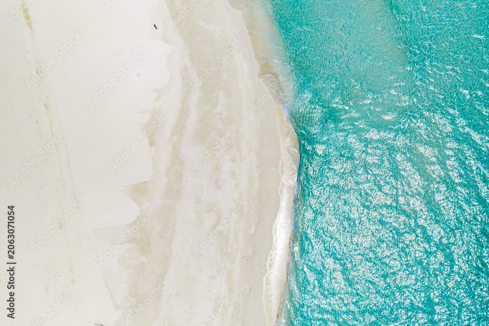 Obraz premium Aerial view of Maldives shoreline shows powder white sand meeting clear turquoise water. Gentle waves shimmer in bright daylight, with sandbars visible and no people present.