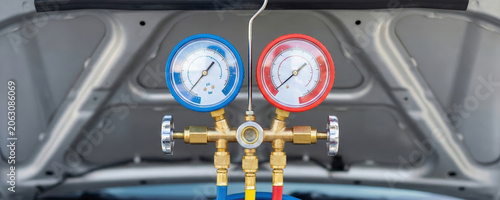 Manifold gauge set with blue and red meters hanging on a car hood for air conditioning system check or refill