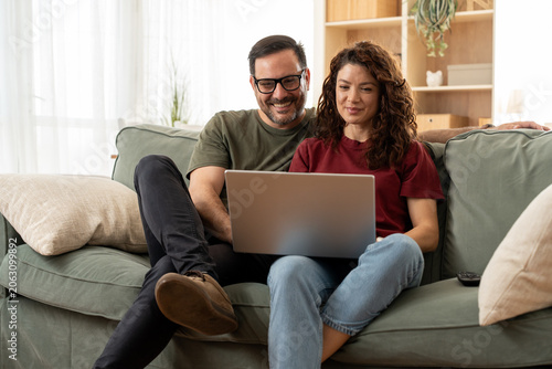 Young couple using laptop together while sitting on sofa at home