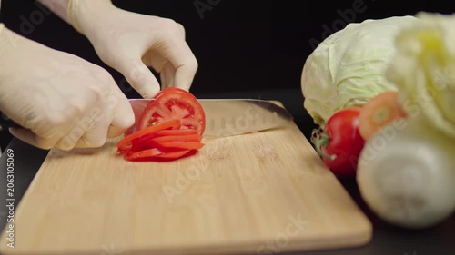 Hands slicing tomato on a wooden cutting board
