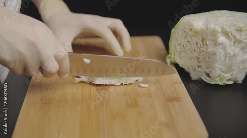 Hands slicing cabbage on a wooden cutting board