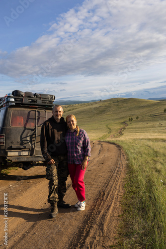 Happy middle aged couple travelers standing on dirt road near off road car safari trip in mongolia steppe landscape