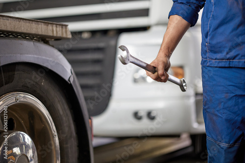 A skilled mechanic wearing blue overalls holds a wrench, standing confidently in front of a truck. This image symbolizes quality workmanship and dedication to automotive care.