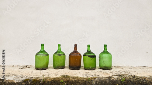 Old glass bottles lined up against a white wall in a minimalist outdoor scene. Concepts of reuse, recycling, sustainable living, and conscious consumption.