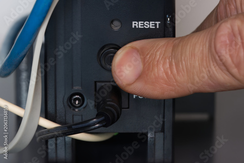 Finger pressing the reset button on the back of the internet router to resolve the home Wi-Fi network issue.