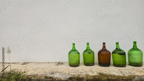 Old glass bottles lined up against a white wall in a minimalist outdoor scene. Concepts of reuse, recycling, sustainable living, and conscious consumption.