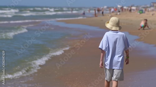 Teenage boy running along the seashore on a warm day. Cheerful guy enjoying a cloudy morning on the seashore. Happy teenager spending summer holidays on a sandy beach.