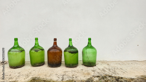 Old glass bottles lined up against a white wall in a minimalist outdoor scene. Concepts of reuse, recycling, sustainable living, and conscious consumption.