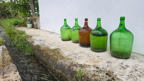 Old glass bottles lined up against a white wall in a minimalist outdoor scene. Concepts of reuse, recycling, sustainable living, and conscious consumption.