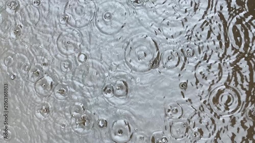 Raindrops falling into water and a puddle, creating circular ripples and small bubbles on the surface. Concept of rainy weather, natural water movement, precipitation, and atmospheric phenomena. Close