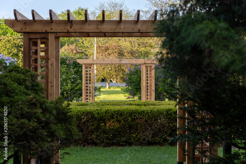 Ornamental Gardens during spring season in Ottawa, Canada. Framed view through wooden garden pergolas and trimmed hedges. Scenic path through wooden arches