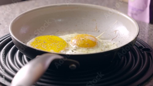 Frying eggs in a pan. Yellow yolks glisten over a lightly cooked white. Pan rests on a black silicone heat absorbing mat.