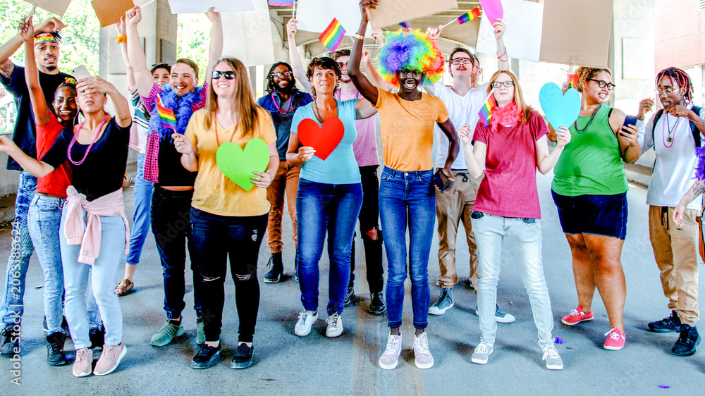 Obraz premium Diverse group of people celebrating with colorful signs and rainbow flags outdoors.