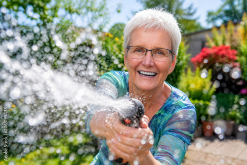 Seniorin mit Wasserschlauch im Garten