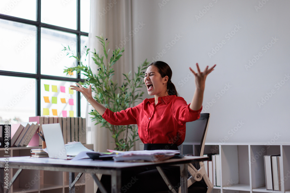Obraz premium Overwhelmed businesswoman expressing intense anger and stress. Raising arms and screaming as papers fly around her desk in a chaotic office. Depicting burnout. Work pressure