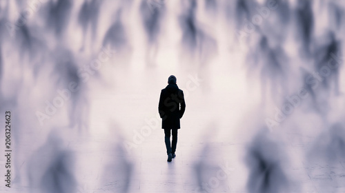 Solitary man walks away, deep within a vast, crowded city street. Surrounding people are blurred, creating a strong sense of isolation and constant movement.