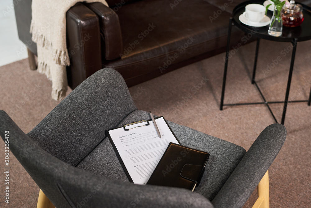 Naklejka premium High angle view of counseling office chair holding intake form and notebook, suggesting adult couple therapy session and mental health support. Useful for psychotherapy marketing and wellness content