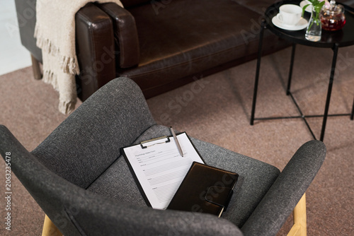 High angle view of counseling office chair holding intake form and notebook, suggesting adult couple therapy session and mental health support. Useful for psychotherapy marketing and wellness content
