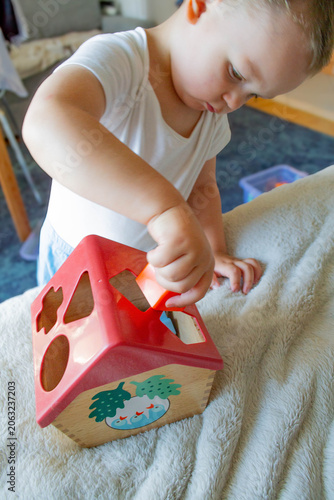 Fotografi A little boy is putting shapes into a wooden sorter shaped like a house