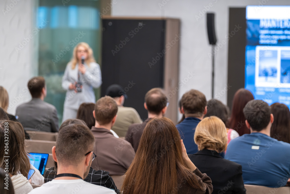 Fototapeta premium Business speaker presenting to engaged audience during conference, attendees listening, taking notes, networking in modern meeting room.