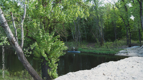 Scenic landscape of a calm forest river with a sandy shore in the foreground and a distant lonely person by the water.