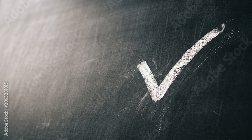 A white chalk check mark drawn on a black chalkboard surface. The drawing is clear and prominent, showcasing a simple yet effective symbol of approval.