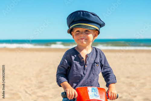 Child enjoys the beach while wearing a police hat and playing with a toy