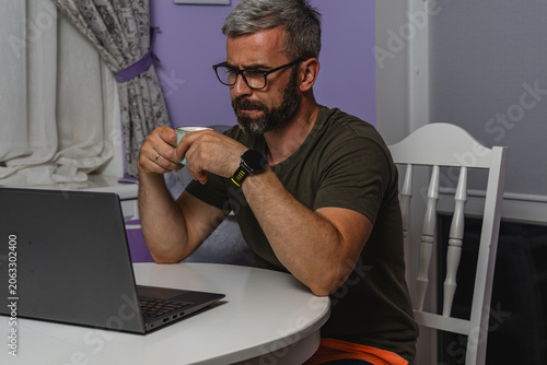 Man enjoying coffee while working on laptop at home during morning hours