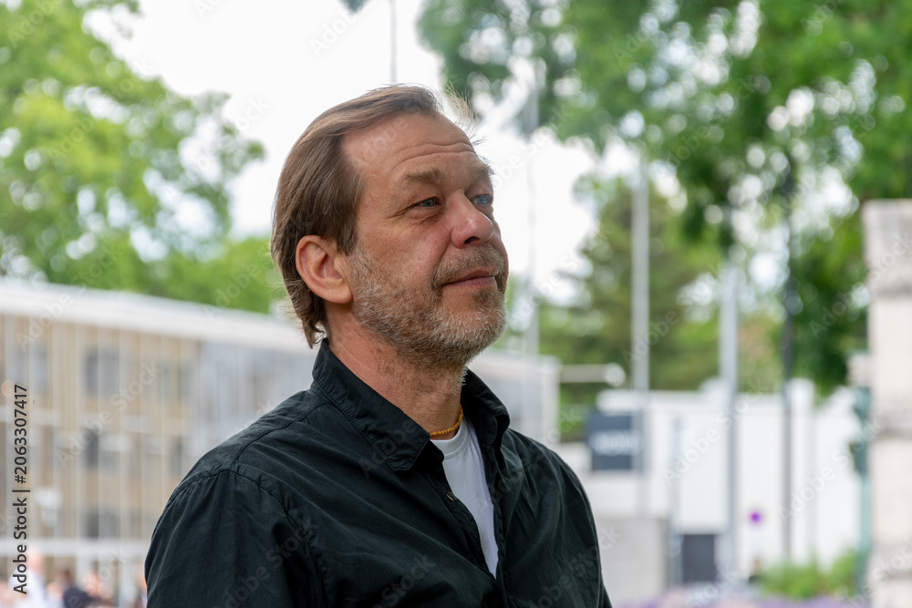 Naklejka premium Man about 55 years old looking into the distance with urban and tree background.