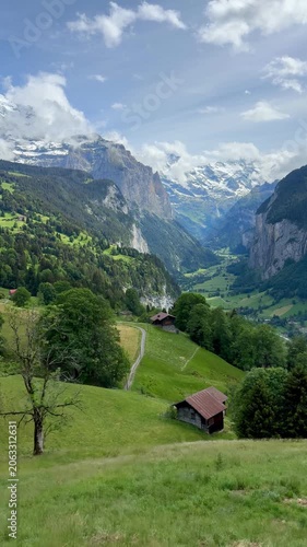 Beautiful alpine valley view with traditional wooden chalets on green grassy hills and majestic snow covered mountain peaks in Lauterbrunnen, Switzerland