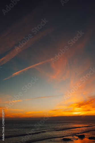 Bright colors fill sky, sun sets over ocean near shore on  warm evening in  coastal area.  sun sets over ocean. Waves roll onto shore as day turns into night. enjoy view on  warm evening by water.
