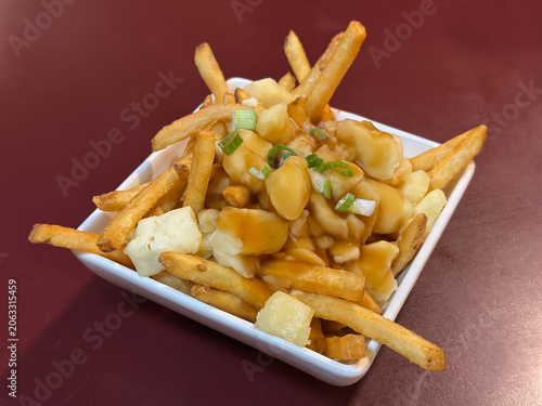 Poutine - consisting of French fries, cheese curds, and brown gravy - is shown on a table in a restaurant. This fast food dish originated in Quebec and has become a fast food staple throughout Canada.