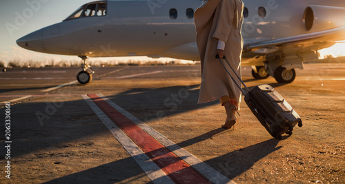 Fotografie Caucasian woman with luggage on airport tarmac in warm sunset light creating a c
