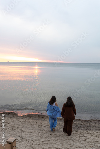 Two girlfriends walk along a sandy beach towards the sea