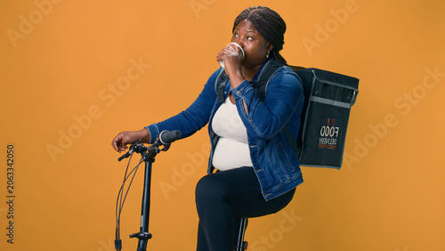 Obraz na plátne Young courier on bicycle takes relaxing moment to enjoy coffee while delivering packages