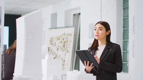 Fotografie In property management office, contractor uses tablet to evaluate and estimate variables as they work with 3D printed architectural prototype, engineer working to design urban area with housing